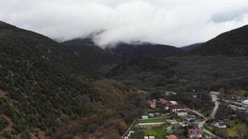 Small town at the foot of the Alps. Stock footage. Aerial view from a drone to the tops of mountains in white clouds. Natural present background. A truck drives by far below, personifying the current video
