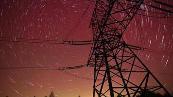A tall power line tower is silhouetted against a vibrant, star-filled sky, capturing the beautiful movement of stars through a long-exposure technique at night. video