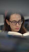 un enfocado joven mujer comprometido en leyendo un libro dentro un moderno y atractivo ajuste video