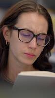 A Focused Individual Wearing Glasses Reading in a Library Surrounded by Books and Knowledge video