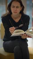 uma pensativo mulher profundamente absorta dentro lendo uma livro dentro uma moderno e convidativo biblioteca video