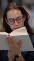 A young woman is engrossed in reading a book in a modern, stylish library environment video