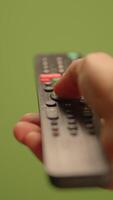 A hand holds a remote control against a vibrant green background enhancing the scene video