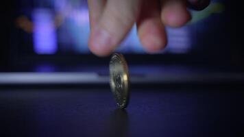 A hand is holding a cryptocurrency coin while trading charts are displayed in the background video