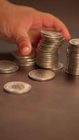 A closeup view of a hand outstretched, reaching for various stacks of coins placed on a table video
