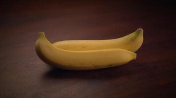 Two fresh bananas sit on a textured wooden surface, illuminated by soft lighting video