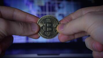 Holding a Cryptocurrency Coin in Front of a Computer Screen Displaying Financial Data video