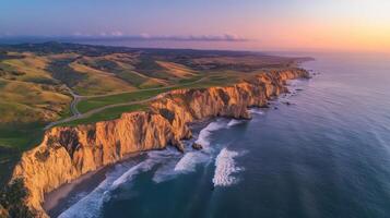 Aerial view of rugged coastal cliffs at sunset with waves and rolling hills photo