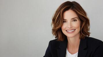 Smiling woman with brown hair in formal attire against neutral background photo
