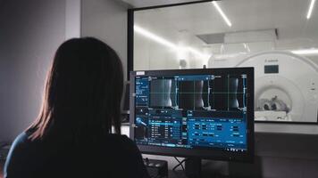 Female Doctor, Radiologist Watching Diagnosis Procedure and Monitors on computer Showing Brain Scans Results, In the Background Patient Undergoes MRI or CT Scan Procedure. video