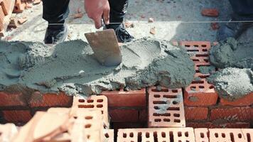 The builder close-up applies a solution of cement on the brick to build the walls of the house of red brick. video