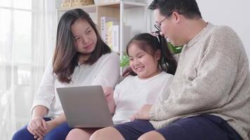 Happy young family with a kid sit on sofa in living room have fun using modern laptop together smiling parents rest on couch enjoy weekend with kid laugh watch video on computer at home
