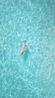 Woman chilling and swims in tropical blue sea. Drone top down view with woman in bikini on vacation, vertical screen video