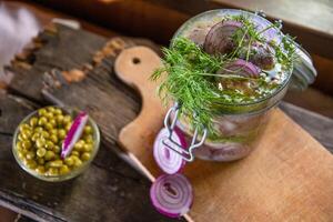 A jar of marinated herring with onions in mustard sauce with dill and green peas on a table in the rays of the sun from the window, rural still life food photo, top view, photo