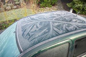 Nature drawings frost patterns on glass and roof of green car at air temperature below zero, abstract winter pattern, photo