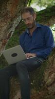 A man is working in a tree while using his laptop, embracing nature and creativity, video