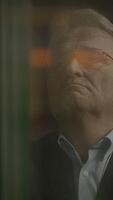 A thoughtful man stands behind glass, bathed in soft light, creating an evocative atmosphere video