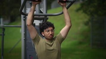 A young man is actively exercising outdoors, making use of pullup bars in a park setting video