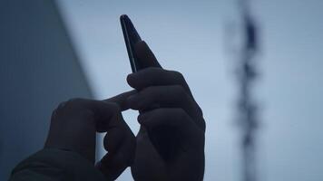 A focused hand is using a smartphone while being in the presence of a communication tower video