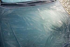 Drawings of nature frost patterns on the hood of a car at temperatures below zero, outside the car on an abstract winter pattern, photo