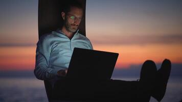 A man is diligently working on his laptop while enjoying a breathtaking scenic sunset background video