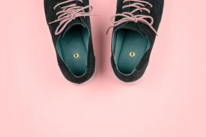 Pair of blue shoes with beige laces featuring push pin placed inside each shoe, against vibrant yellow background with copy space. Pranks and tricks concept photo