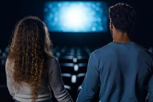 A romantic moment of a couple holding hands in a dimly lit movie theater, facing a glowing screen with a bokeh effect, creating a cozy and intimate atmosphere photo