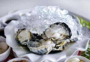 Fresh oysters half shell on ice with lime wedges and other side dishes, spicy Thai style, seafood meal from the sea, local food photo
