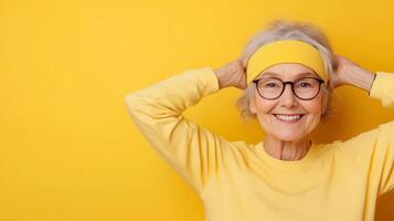 Smiling elderly woman in yellow outfit with headband standing against yellow background. Copy Space photo