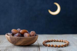 Traditional wooden bowl of dates and prayer beads under a crescent moon photo