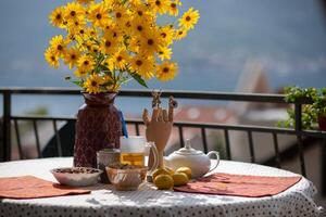 Bright yellow flowers in a vase on a table set with colorful dishes and a scenic backdrop creates a warm atmosphere for morning tea on a sunny day photo