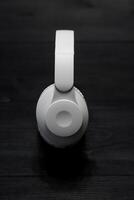 White over-ear headphones on a dark wooden surface, top view, minimalistic design, modern technology, isolated object, suitable for music and audio-related themes. photo