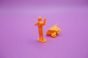 wheelbarrow toy and miniature worker isolated on purple background. yellow wheelbarrow and toy workers raising their hands. photo