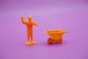 Miniature Worker Figures and Yellow Wheelbarrow on Purple Background photo