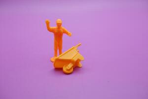 Toy Workers with Yellow Wheelbarrow Isolated on Purple Backdrop photo