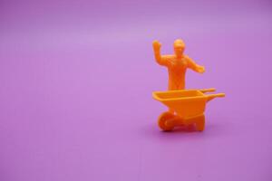 Toy Workers and Yellow Wheelbarrow Displayed on Purple Background photo