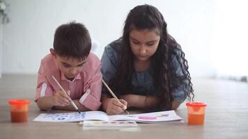 Happy little brother and sister paint with colors in the album lying on the floor in a good mood and smiling. video
