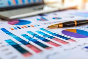 Pen resting on financial charts displaying business performance with laptop in background photo