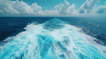 Ocean wake pattern stretches behind cruise ship in aerial view. Deep blue sea meets bright sky with white clouds, while turquoise foam trails create dynamic water movement on sunny day. sunny photo
