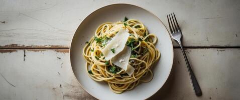 Freshly prepared spaghetti with herbs and cheese served on a white plate with fork on a rustic wooden table. photo