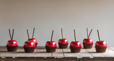 Shiny red candy apples with chocolate cupcake bases on a wooden table. photo