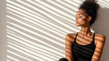 fit woman in black outfit poses gracefully, illuminated by soft shadows photo