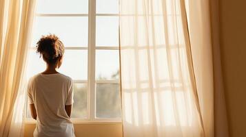 woman gazes out window, framed by soft curtains, reflecting on life photo