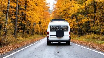 camper van driving on road surrounded by vibrant autumn trees photo