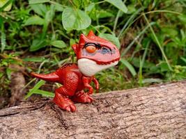 A toy dinosaur is sitting on a log photo