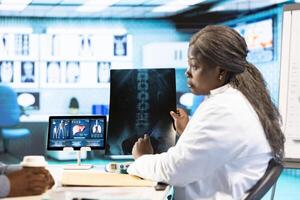 General practitioner reviewing x ray imaging at checkup with male patient, offering her professional expertise to ensure wellness. Medic doing scan interpretation with a man in the office. photo