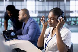 Engineer in data center listening songs while using system monitoring software on computers to identify errors. Woman wearing headphones, enjoying music in server farm, repairing infrastructure photo
