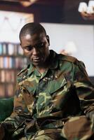 African american army veteran in camouflage clothing sits in therapy, looking distressed and sharing feelings about combat scenes. War soldier dealing with PTSD, reintegration program. photo