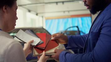 Salesperson in auto showroom discussing with man, offering color swatch samples choice. Agent providing client with color wheel selection, picking hue for car paint, camera B close up photo