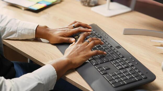 Person at home office desk typing on PC keyboard next to coffee mug, close up shot. Remote employee in apartment pressing computer peripheral keys, inputting data, camera B photo